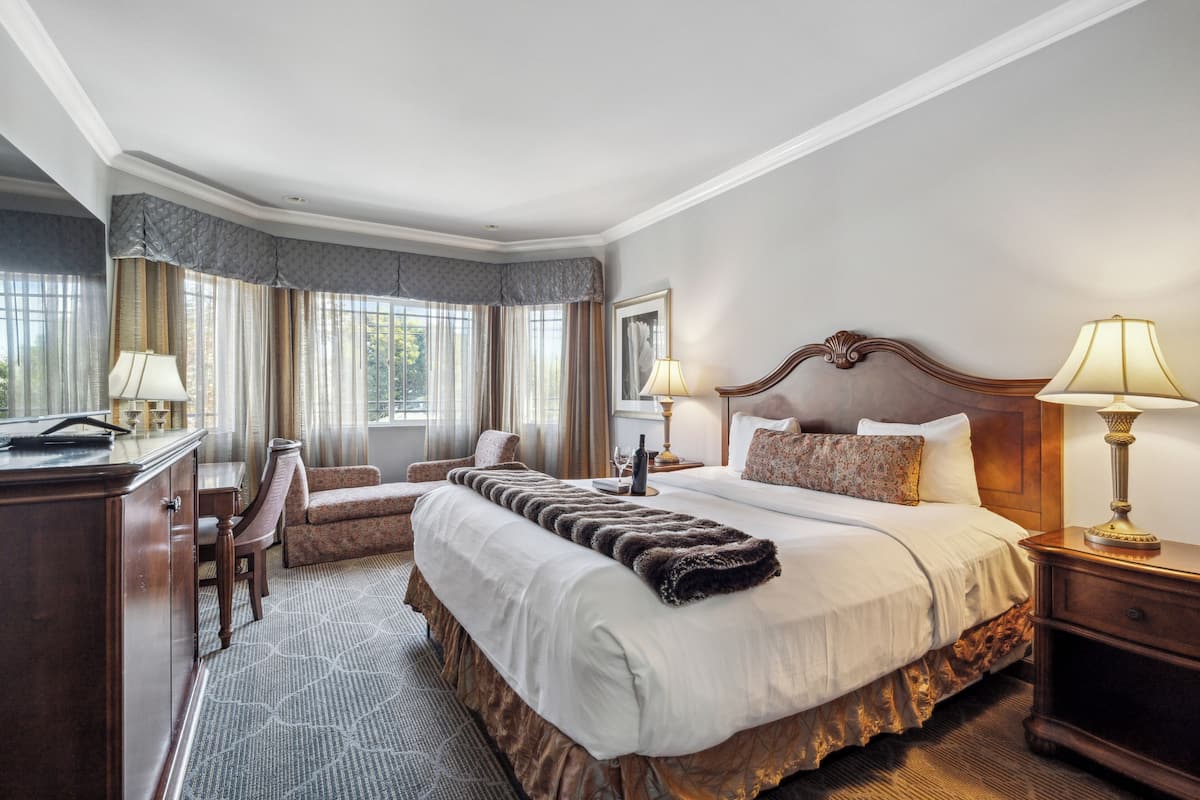 A hotel room with a large bed, a desk, a chair, and a lamp.