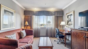 Una habitación de hotel con sofá, escritorio, silla, armario y ventana con cortinas.