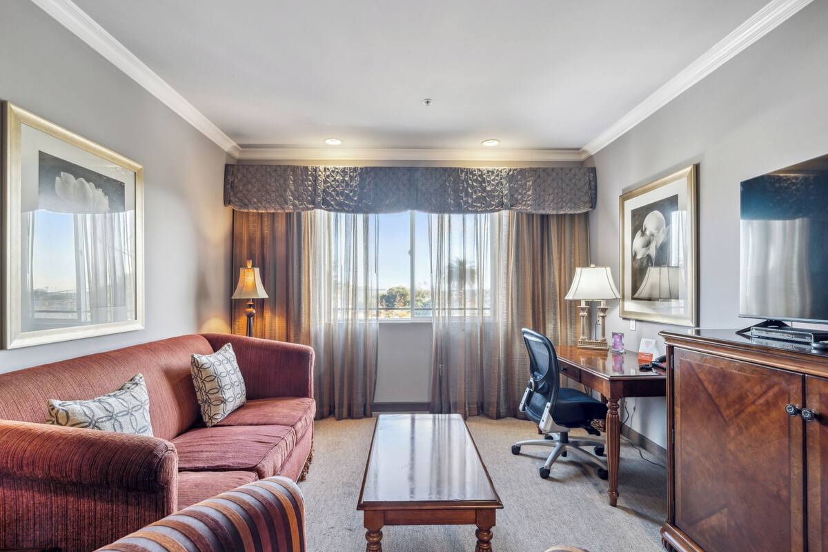 A hotel room with a sofa, a desk, a chair, a cabinet, and a window with curtains.