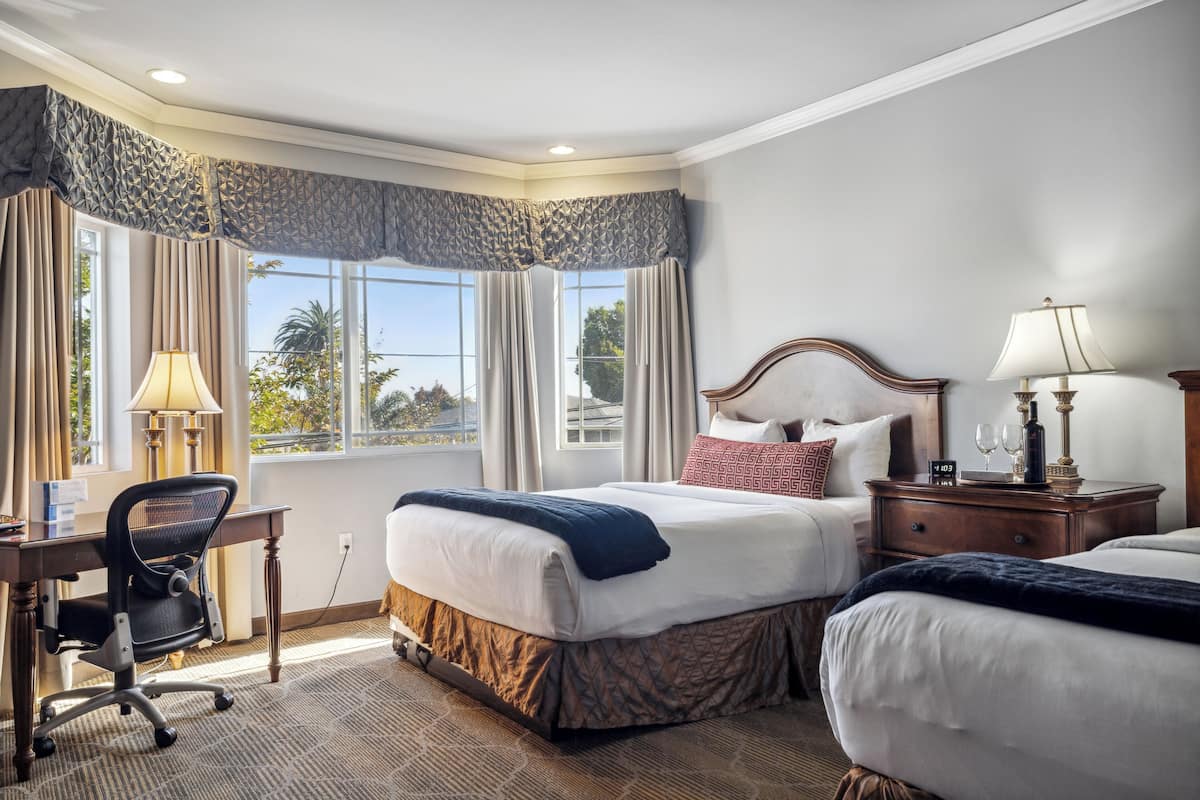 A hotel room with a large bed, a desk with a chair, a nightstand with a lamp, and a view of the outdoors through the window.