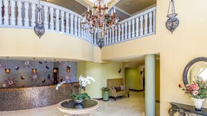 Un vestíbulo amplio con techos altos, una imponente escalera, un mostrador de recepción y un candelabro decorativo.