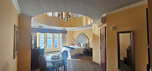 Una habitación de hotel con una cama grande, una mesa de comedor, una araña y vistas de la ciudad a través de las ventanas.