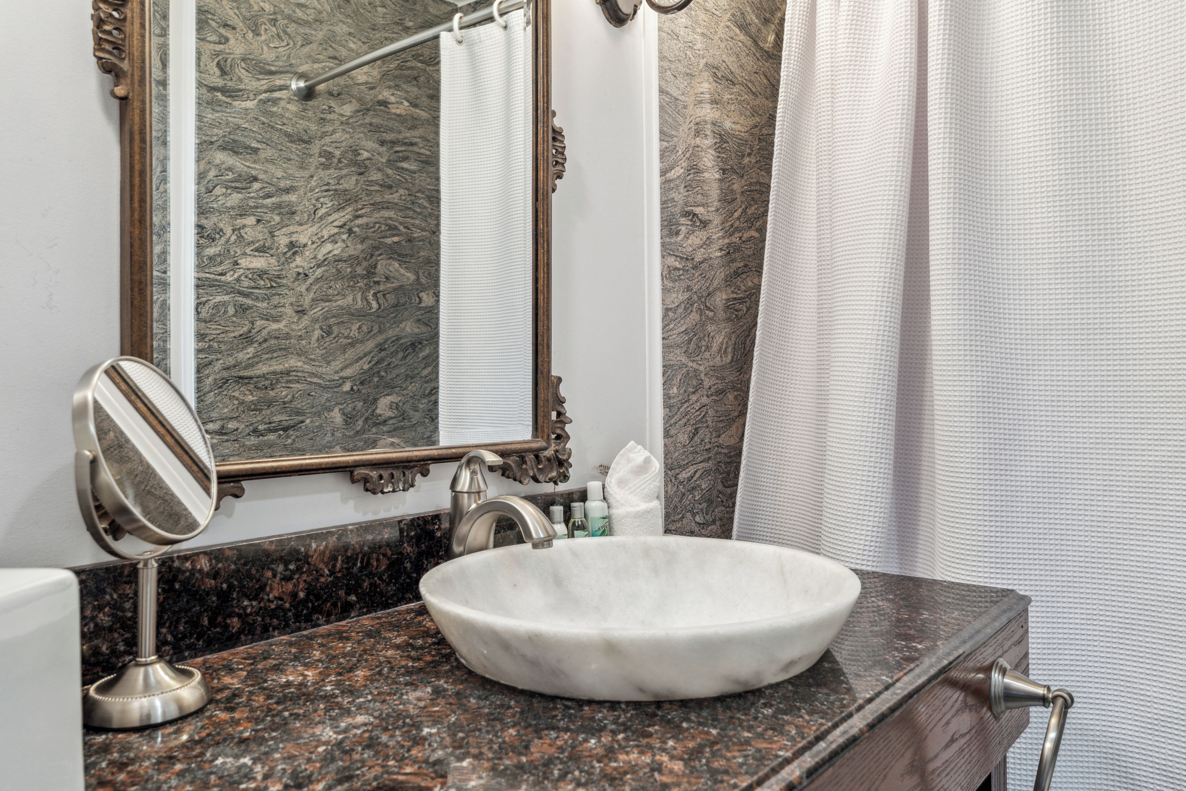 A bathroom with a marble sink, a mirror, and a shower curtain.