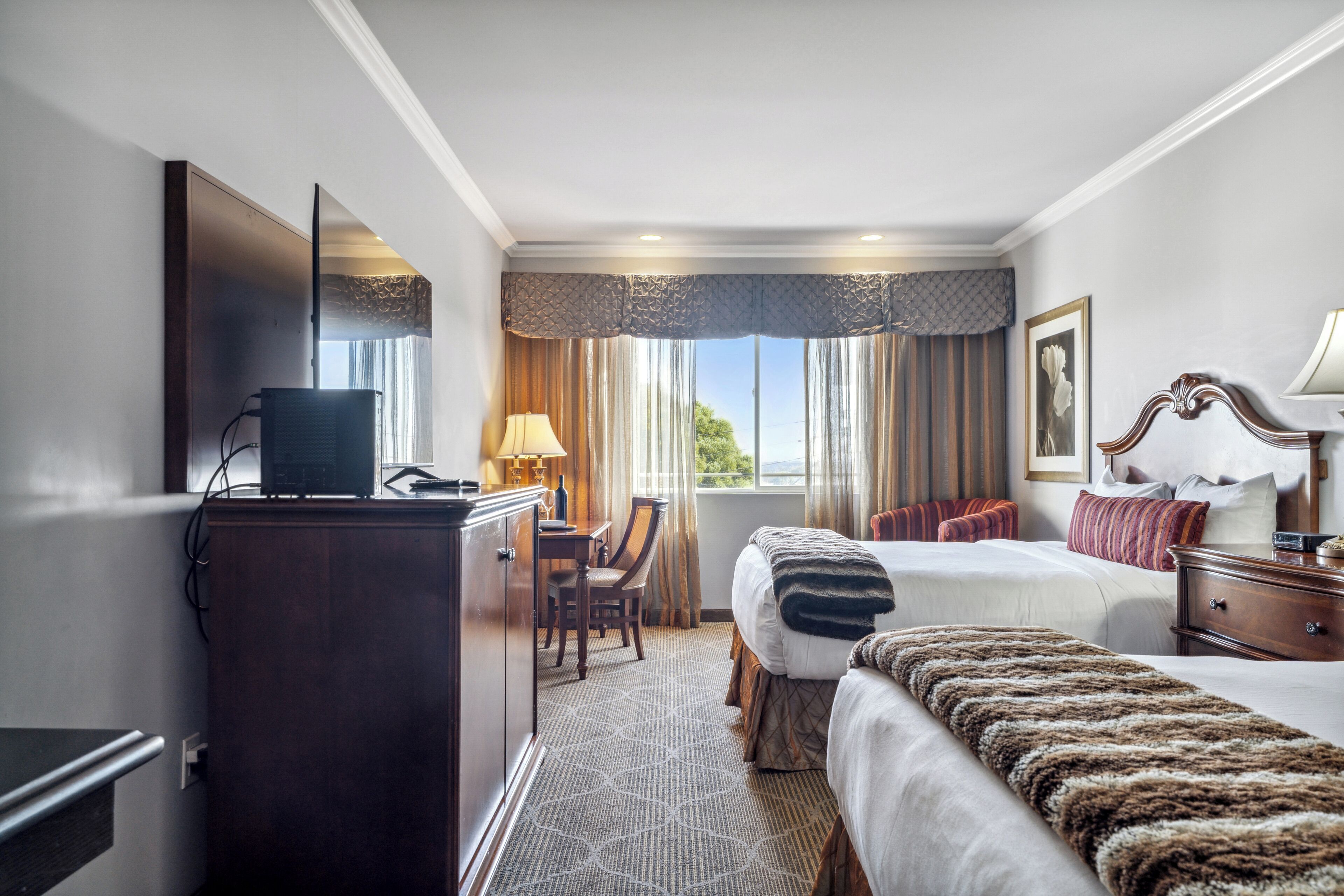 A hotel room with a bed, a desk with a computer, a television, and a window with curtains.