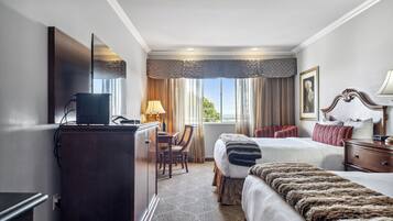 A hotel room with a bed, a desk with a computer, a television, and a window with curtains.