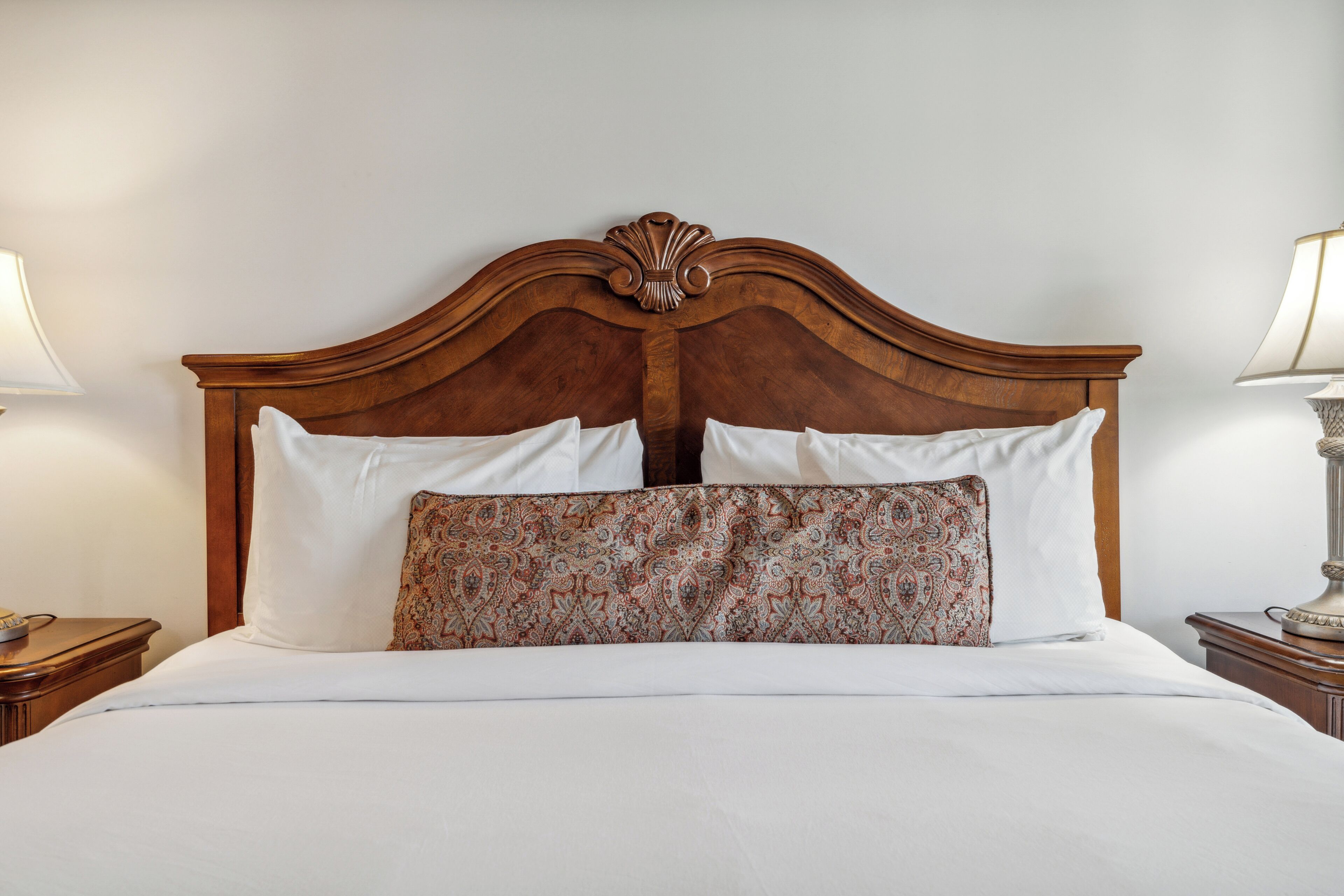 Un lit bien fait, avec une tête de lit en bois, une literie blanche et un coussin à motifs.