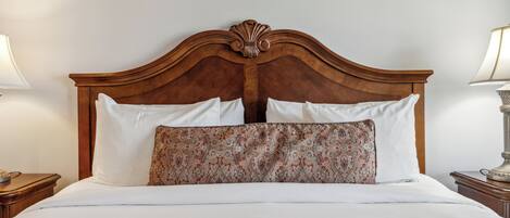 Un lit bien fait, avec une tête de lit en bois, une literie blanche et un coussin à motifs.