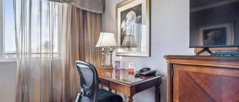 A hotel room with a desk, chair, lamp, telephone, and a television.