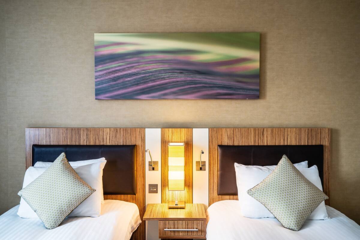 A hotel room with two beds, a wooden headboard, a nightstand, and a wall-mounted artwork.