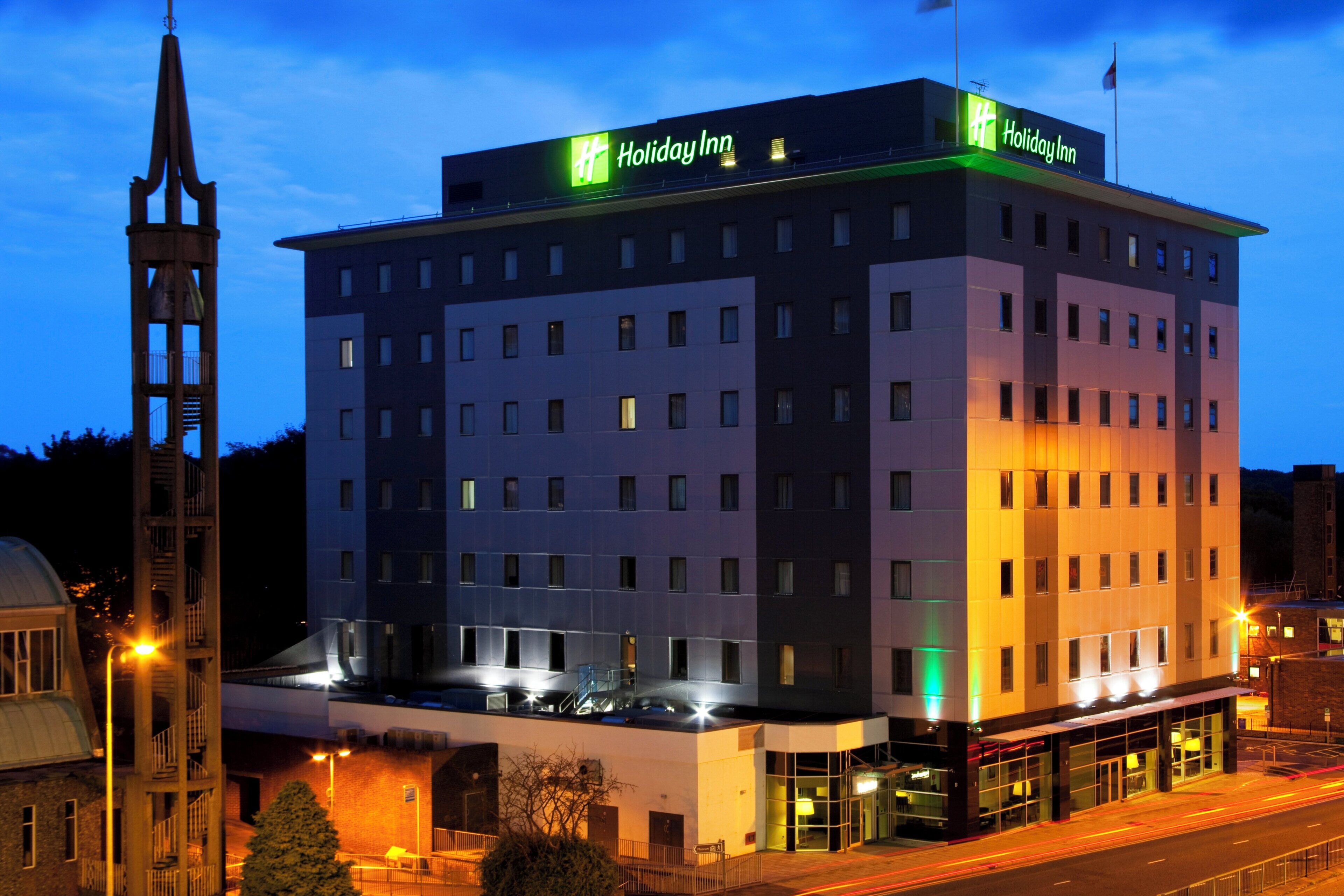 Een Holiday Inn hotel met een modern design, met een opvallende toren en een goed verlichte gevel.