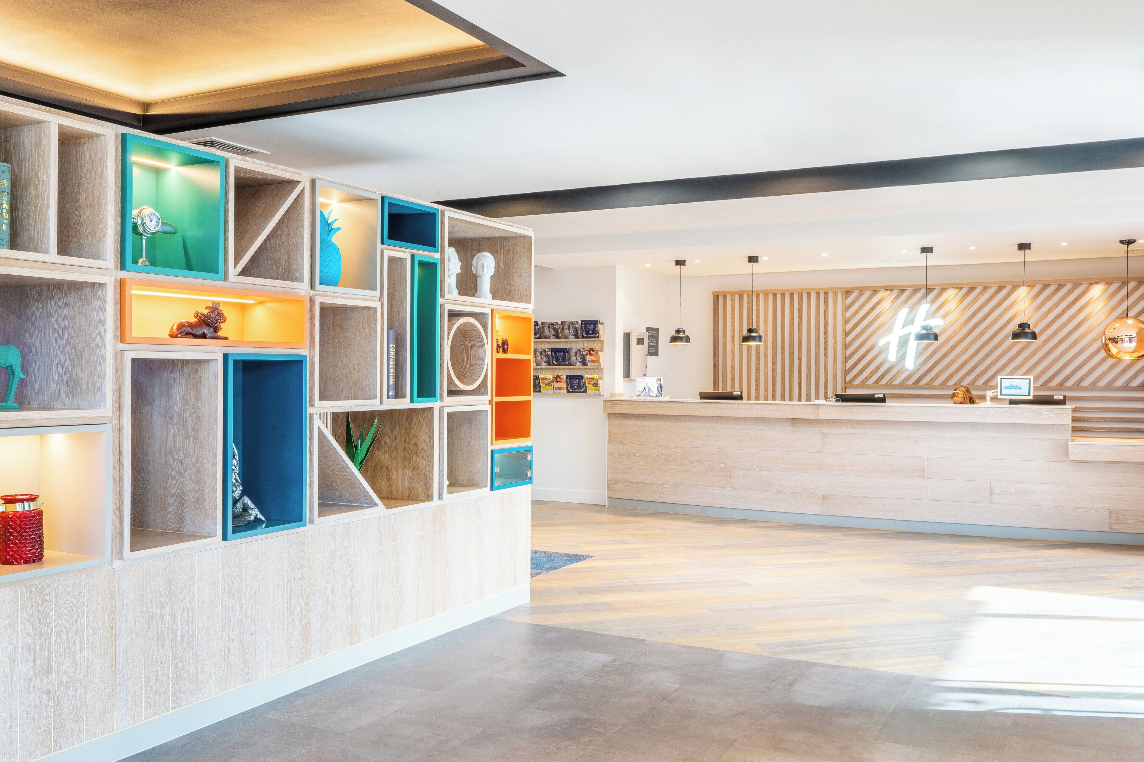A modern reception area with a wooden reception desk, a colorful shelving unit with various decorative items, and a striped wooden wall in the background.