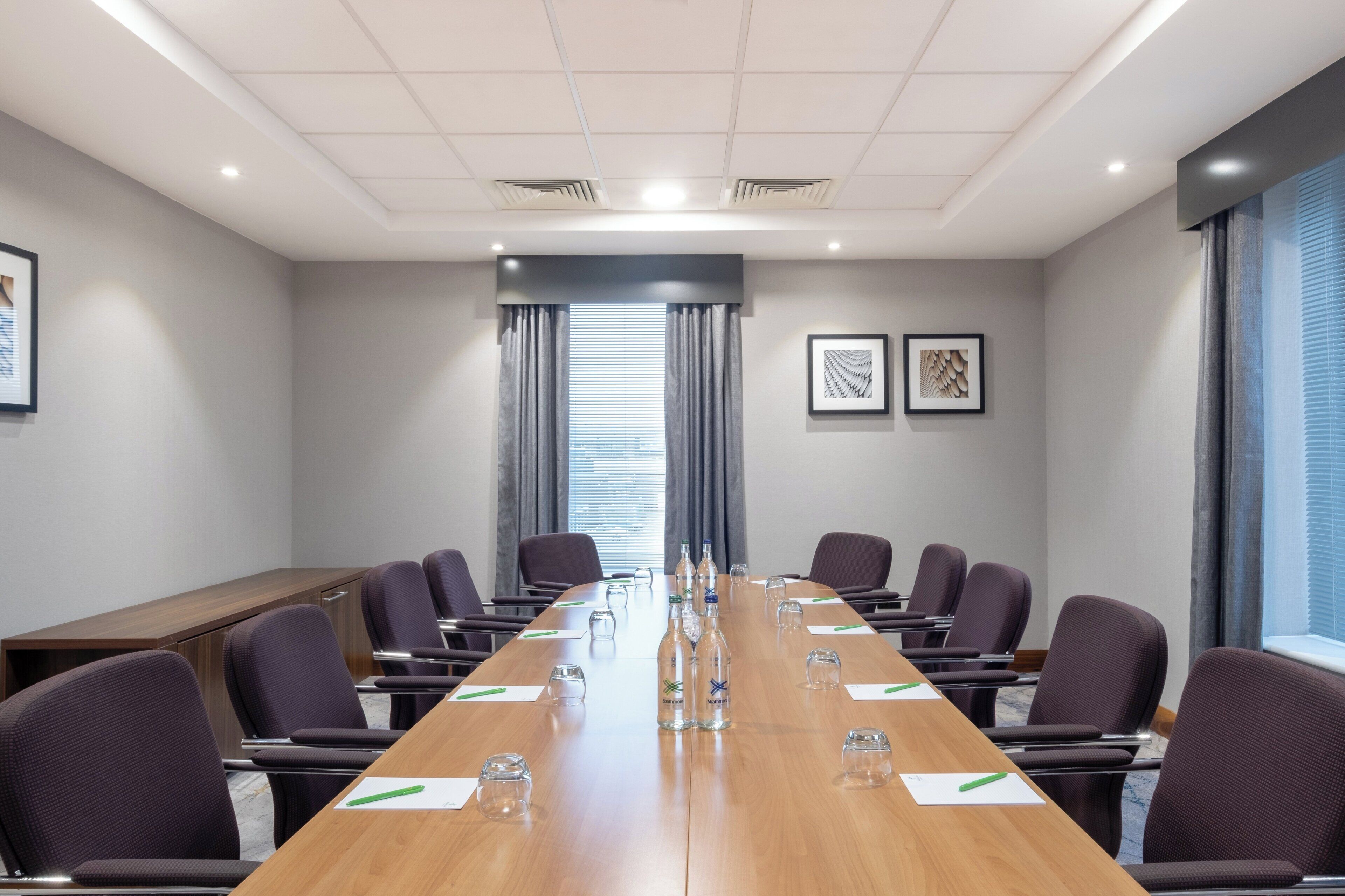 Un salón de conferencias con una larga mesa, sillas y una ventana con persianas.