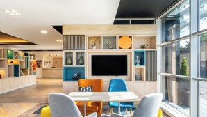 A modern living room with a large TV, colorful furniture, and a view through large windows. - Holiday Inn Stevenage by IHG (Stevenage)