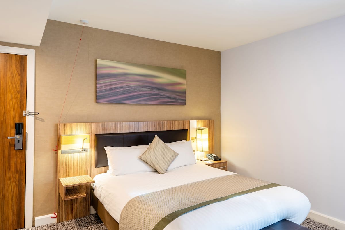 A neatly made bed with a headboard, bedside lamps, and a wall-mounted artwork.