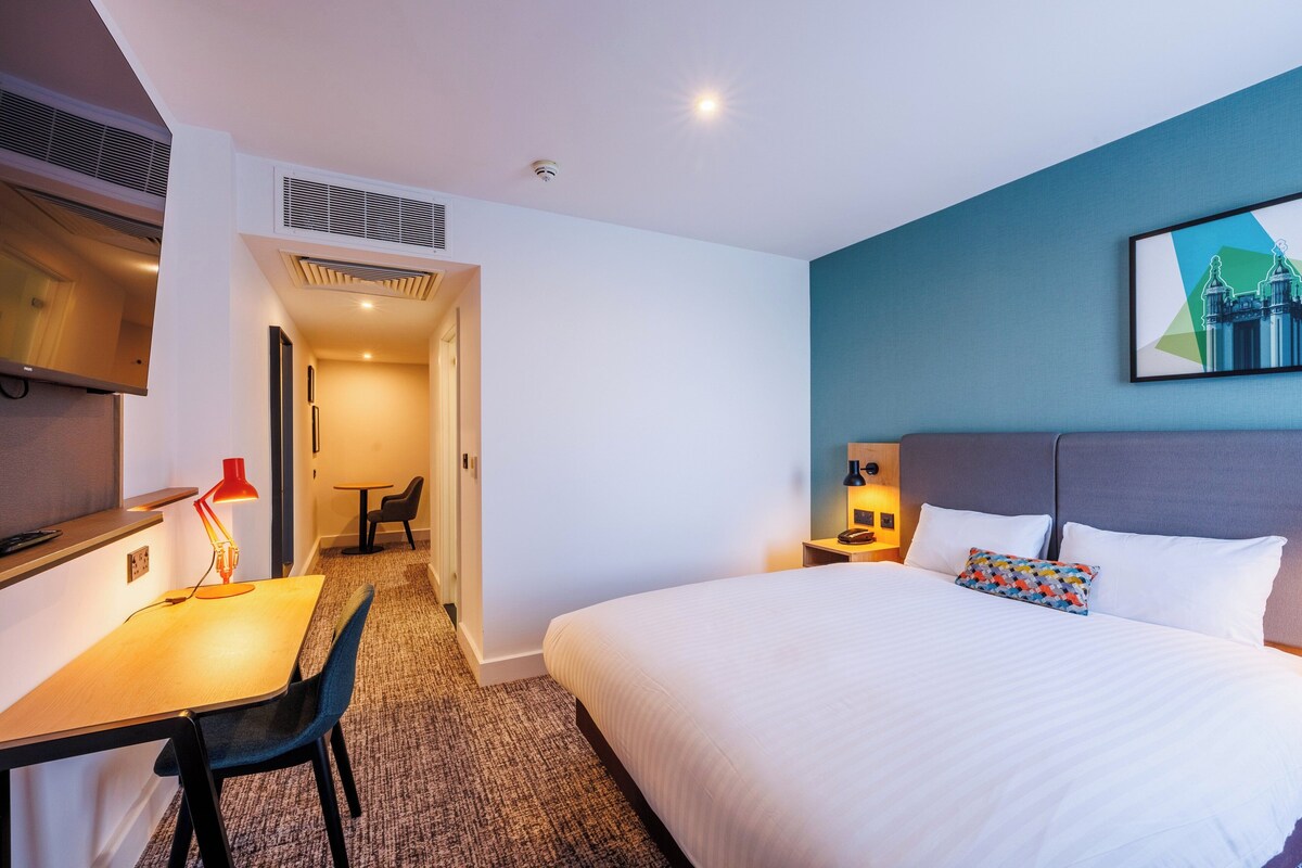 Habitación de hotel con cama, escritorio, silla y un cuadro en la pared.