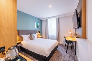 A hotel room with a bed, a desk, a chair, a television, and a coffee maker.