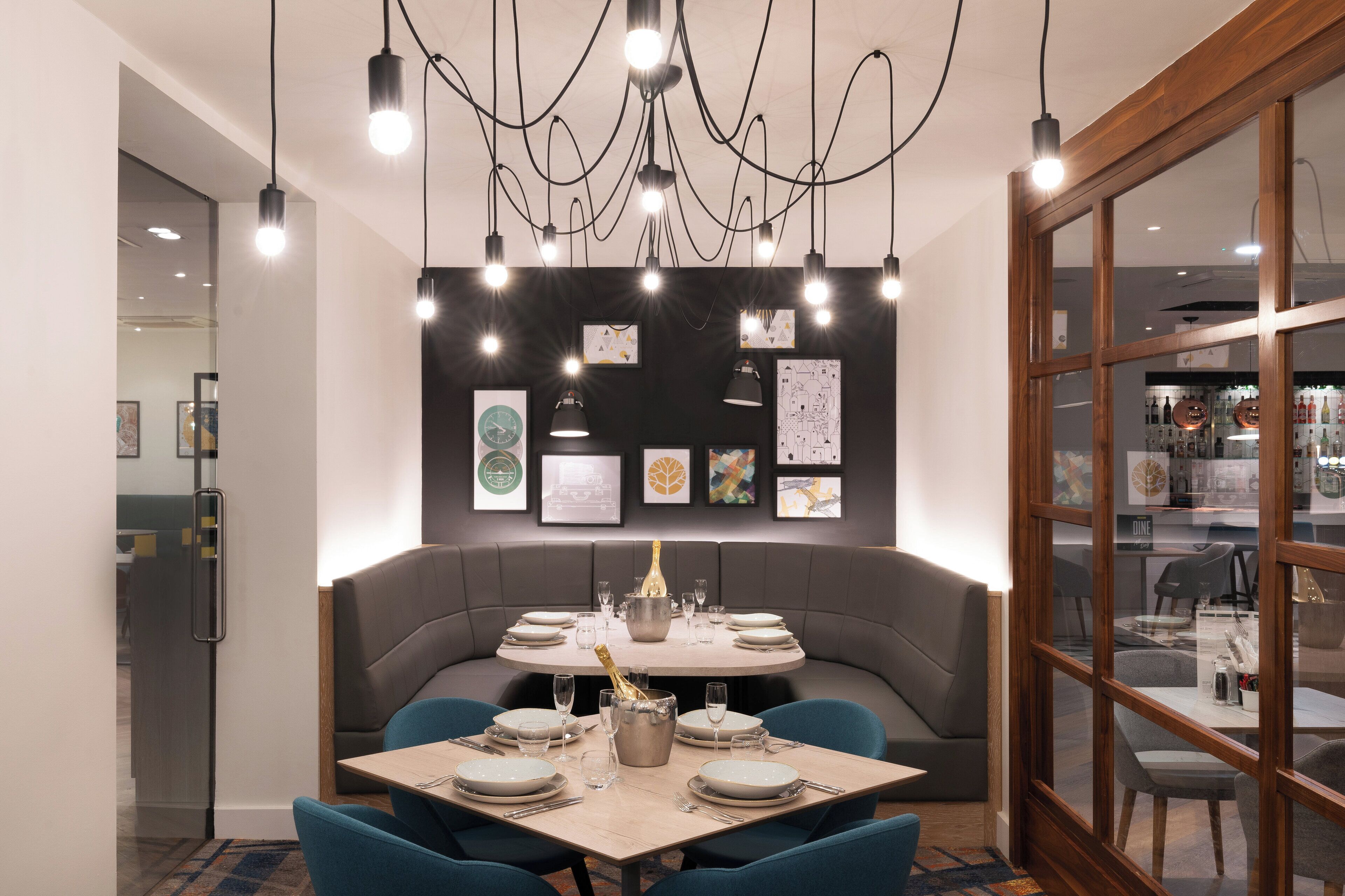 A modern dining area with a round table set for six, a champagne bottle, and a variety of framed artwork on the wall.