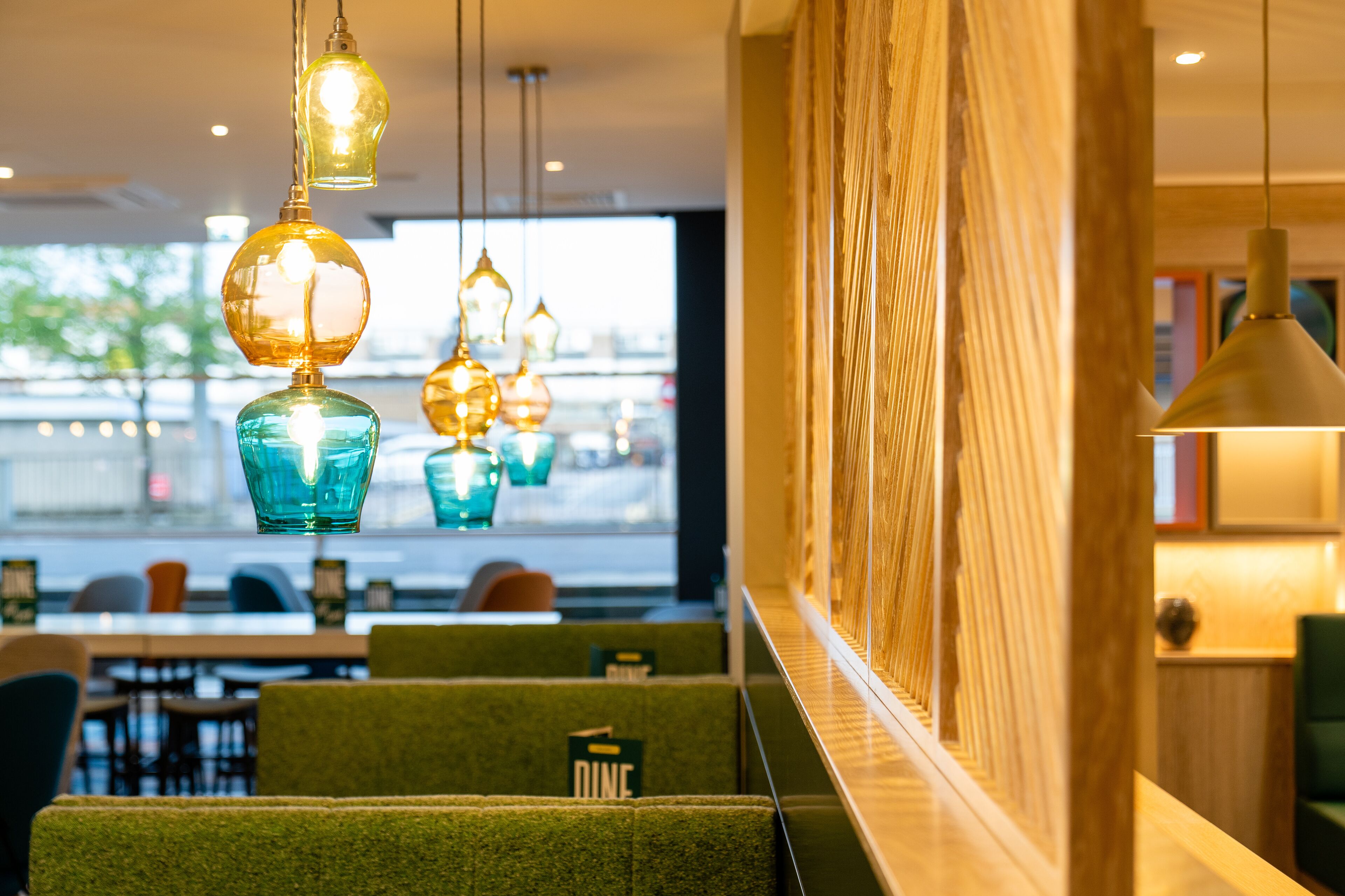 A restaurant with green upholstered booths, hanging pendant lights, and a view of the street through large windows.