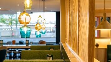 A restaurant with green upholstered booths, hanging pendant lights, and a view of the street through large windows.