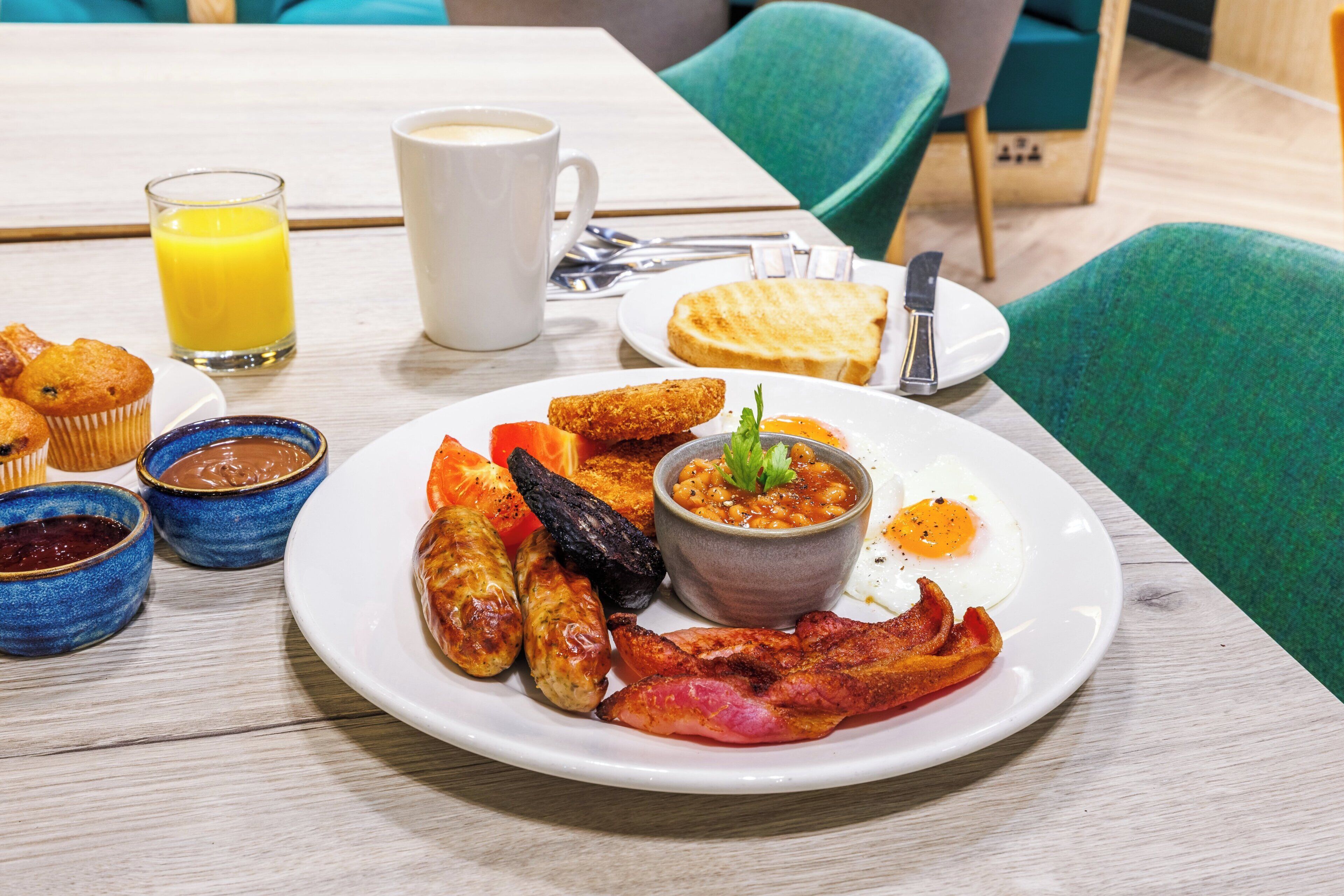 A breakfast plate with eggs, bacon, sausages, toast, and a bowl of beans.
