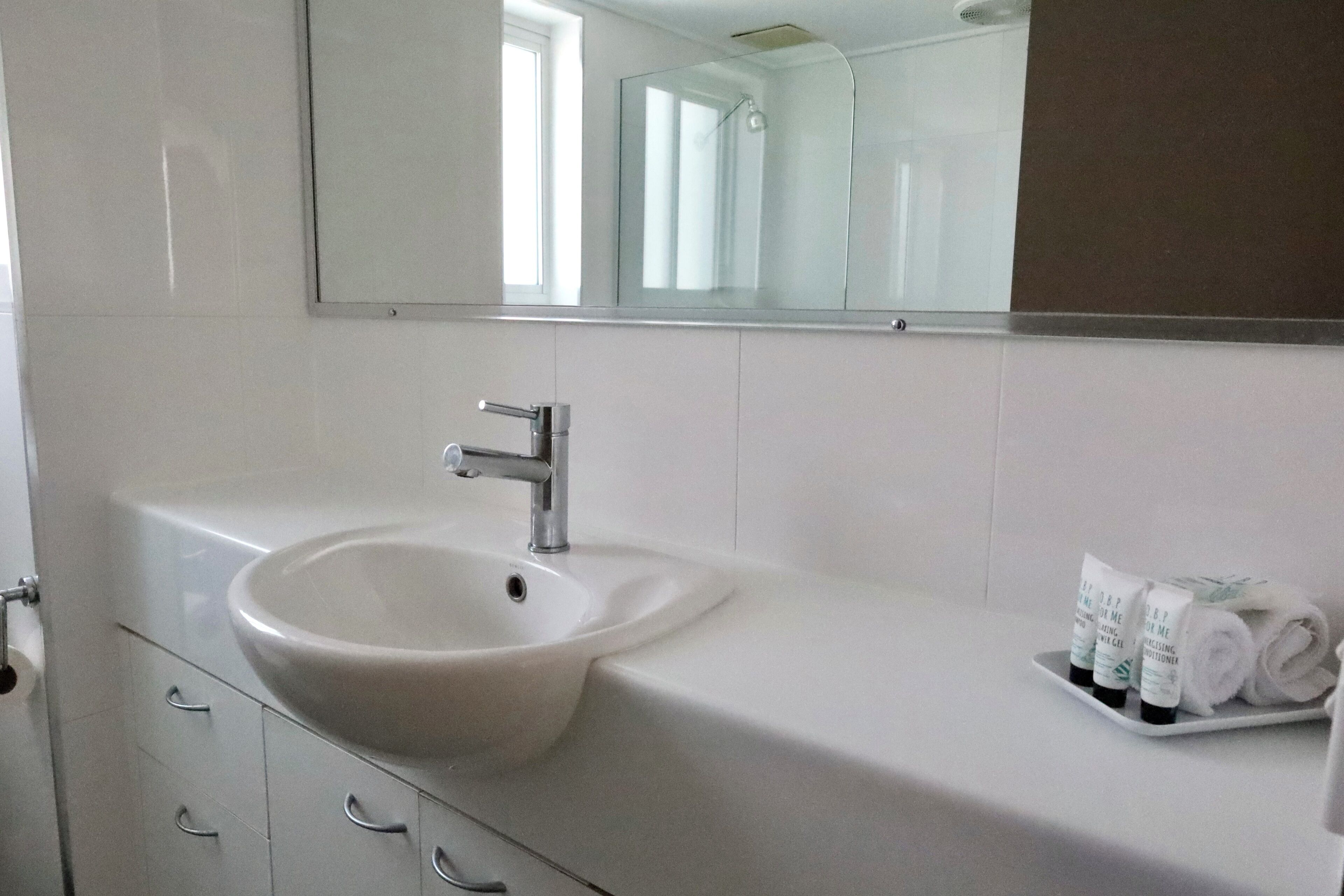 A bathroom with a white sink, a mirror, and a tray with toiletries.