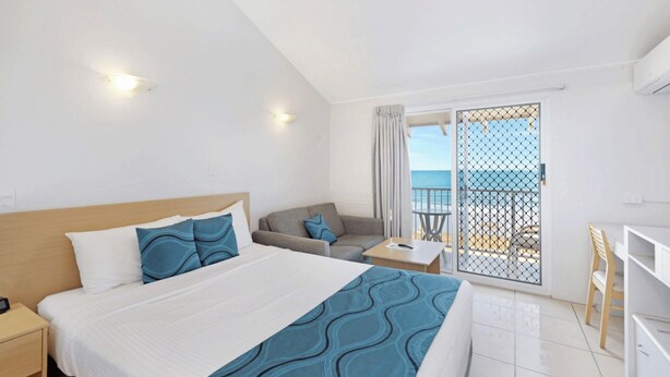 A hotel room with a bed, a sofa, a small table, and a balcony with a view of the sea. - Don Pancho by the Beach (Bargara)