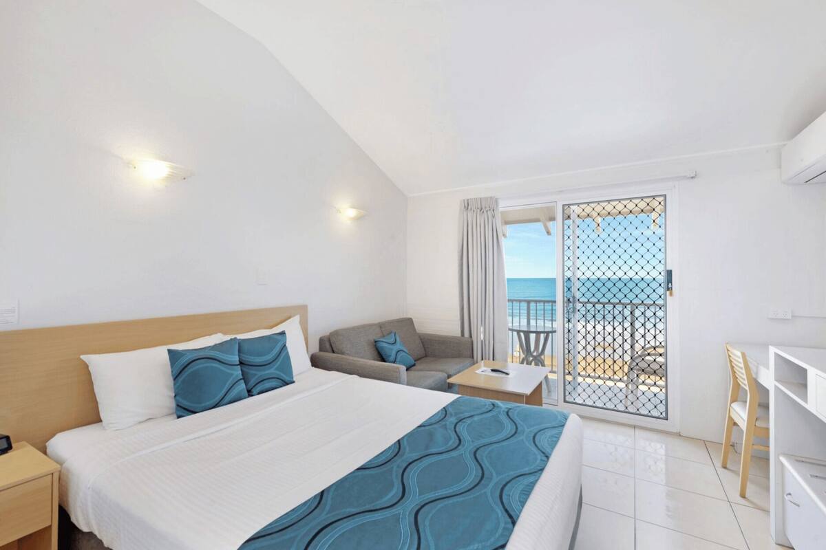 Een hotelkamer met een bed, een bank, een tafeltje en een balkon met uitzicht op zee.