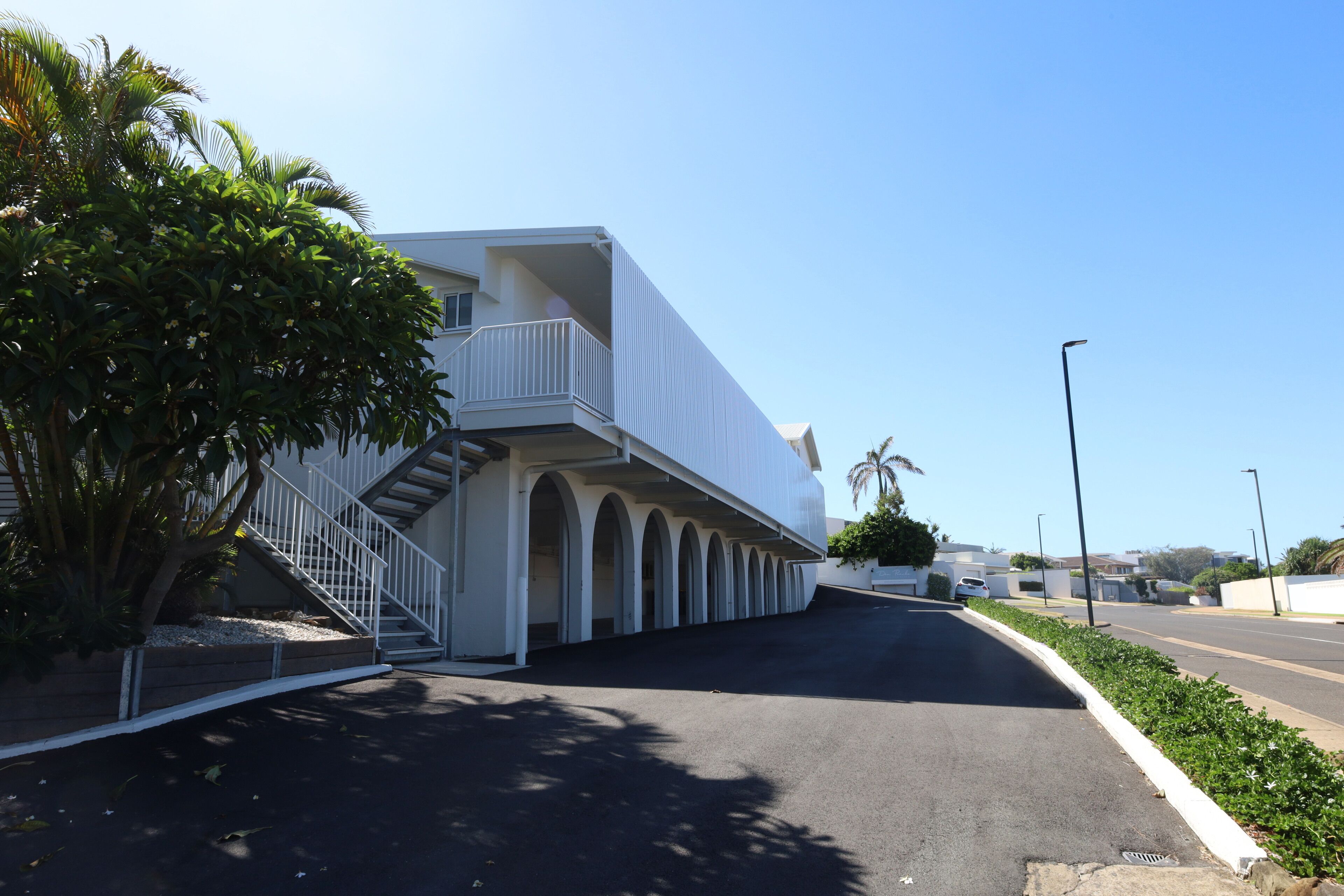 A modern building with a white exterior, a balcony, and a staircase leading to the entrance.