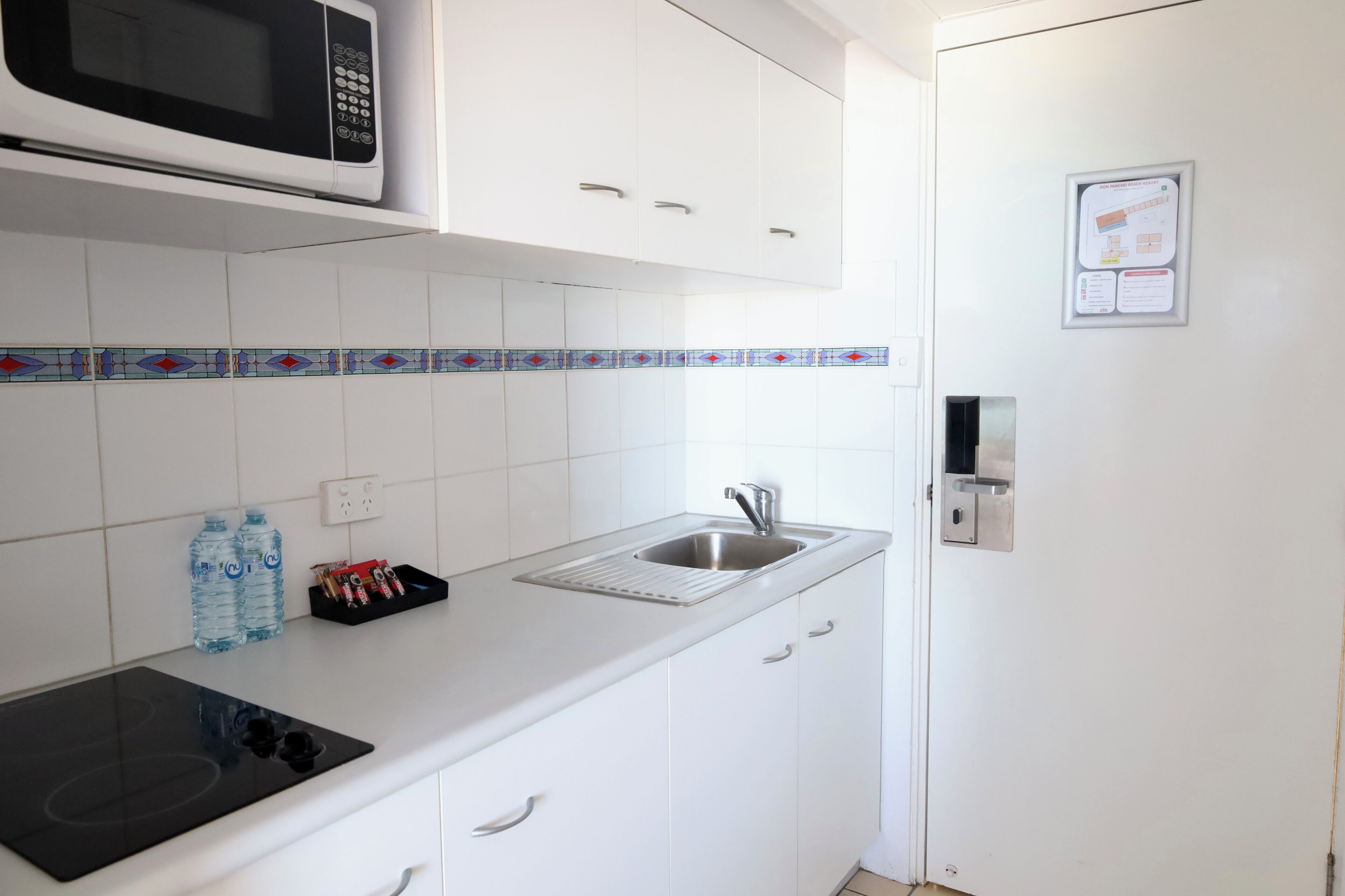 A kitchen with white cabinets, a microwave, a sink, and a tiled backsplash.