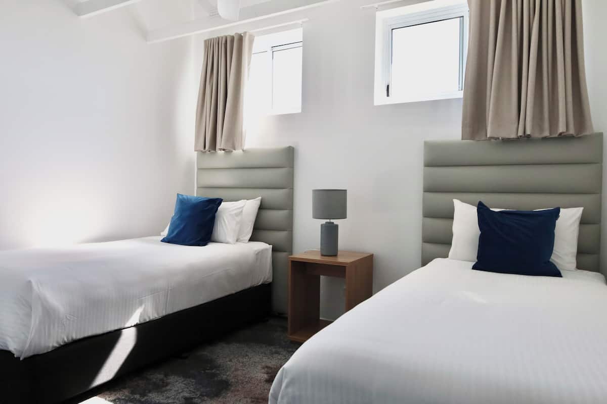 Een hotelkamer met twee bedden, een klein tafeltje met een lamp en een raam met gordijnen.