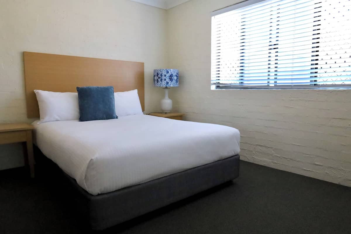 Een hotelkamer met een groot bed, een nachtkastje met een lamp en een raam met zonwering.