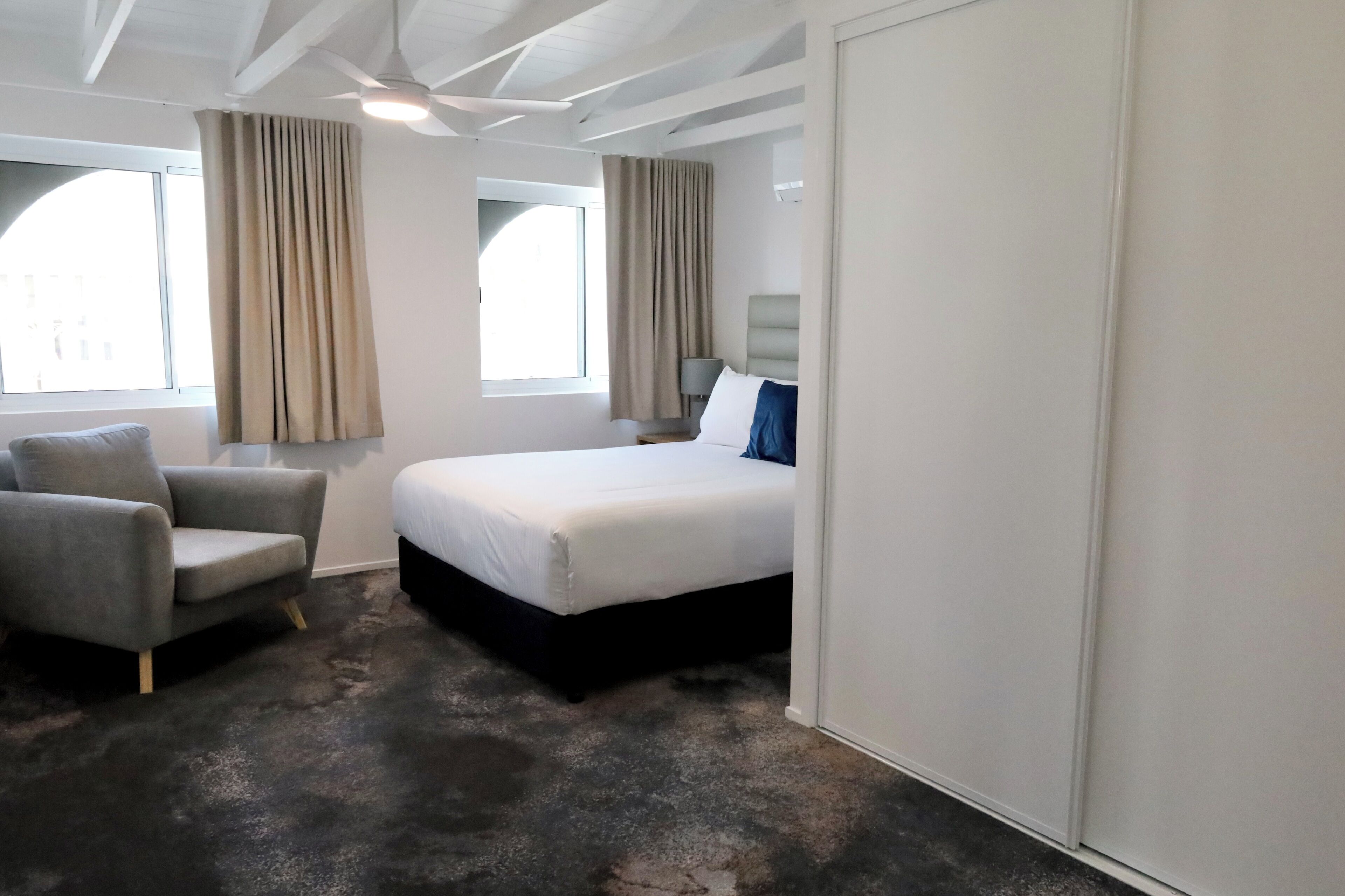 A hotel room with a bed, a chair, a lamp, and a window with curtains.