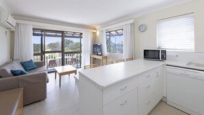A modern kitchen with a central island, a dining area with a table and chairs, a sofa, and a view of the outdoors through large windows. - Don Pancho by the Beach (Bargara)