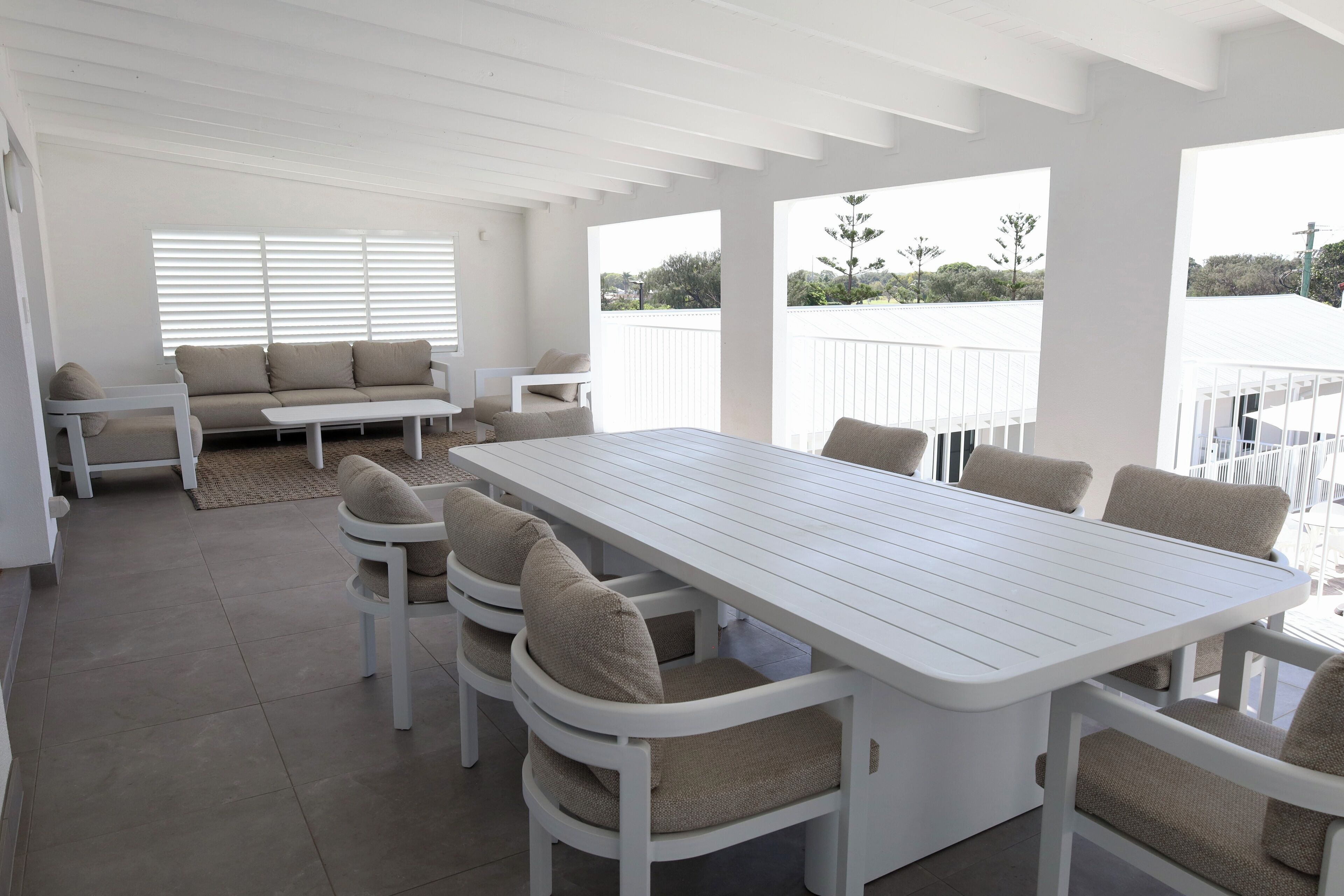 A covered patio area with a white table and chairs, a sofa, and a view of the surrounding landscape.