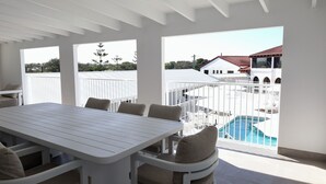 A spacious balcony with a pool, white furniture, and a view of a building with a red roof. - Don Pancho by the Beach (Bargara)