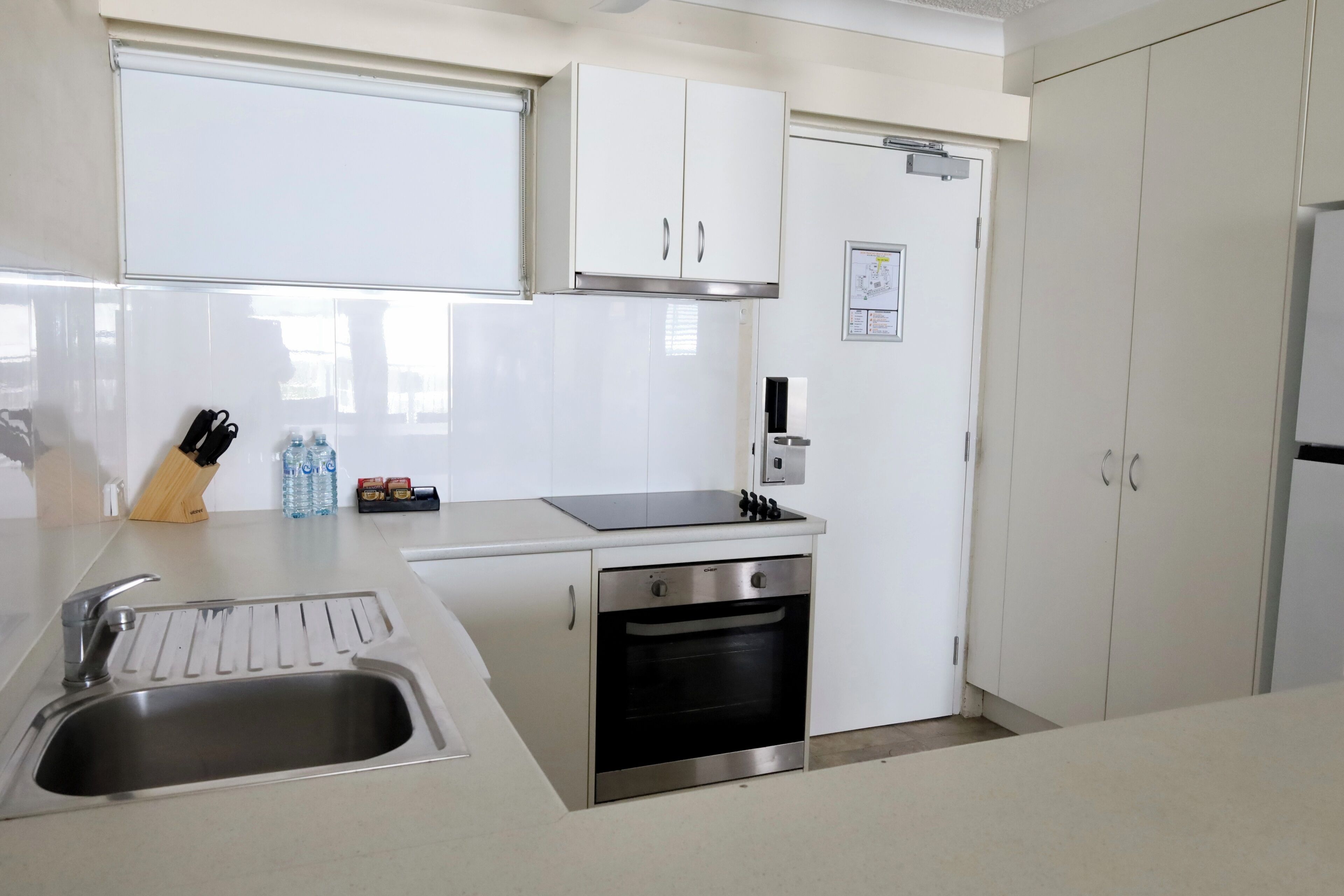 A modern kitchen with white cabinets, a stainless steel sink, a built-in oven, and a window above the sink.
