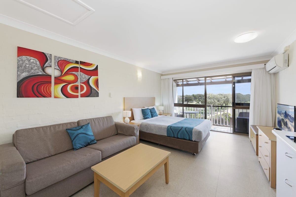 Een moderne hotelkamer met een bank, twee bedden, een televisie en een balkon met uitzicht.