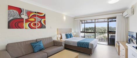 Una habitación de hotel moderna con sofá, dos camas, televisor y balcón con vistas.