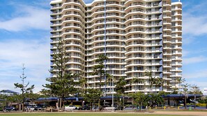 Un hôtel à plusieurs étages, doté d’une façade incurvée, de balcons et d’un espace de stationnement à l’avant.