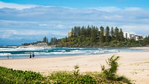 Une plage avec des vagues, des gens et des bâtiments en arrière-plan.