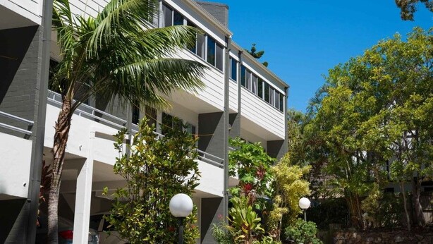 A modern building with a white facade, multiple balconies, and lush greenery including palm trees. - Palm Court Noosa (Noosa Heads)