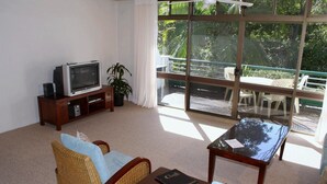 A living room with a television, wicker furniture, a glass table, and a balcony with outdoor seating. - Palm Court Noosa (Noosa Heads)