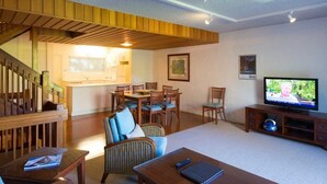 A spacious living area with a wooden staircase, a dining table with chairs, a television, and a sofa. - Palm Court Noosa (Noosa Heads)