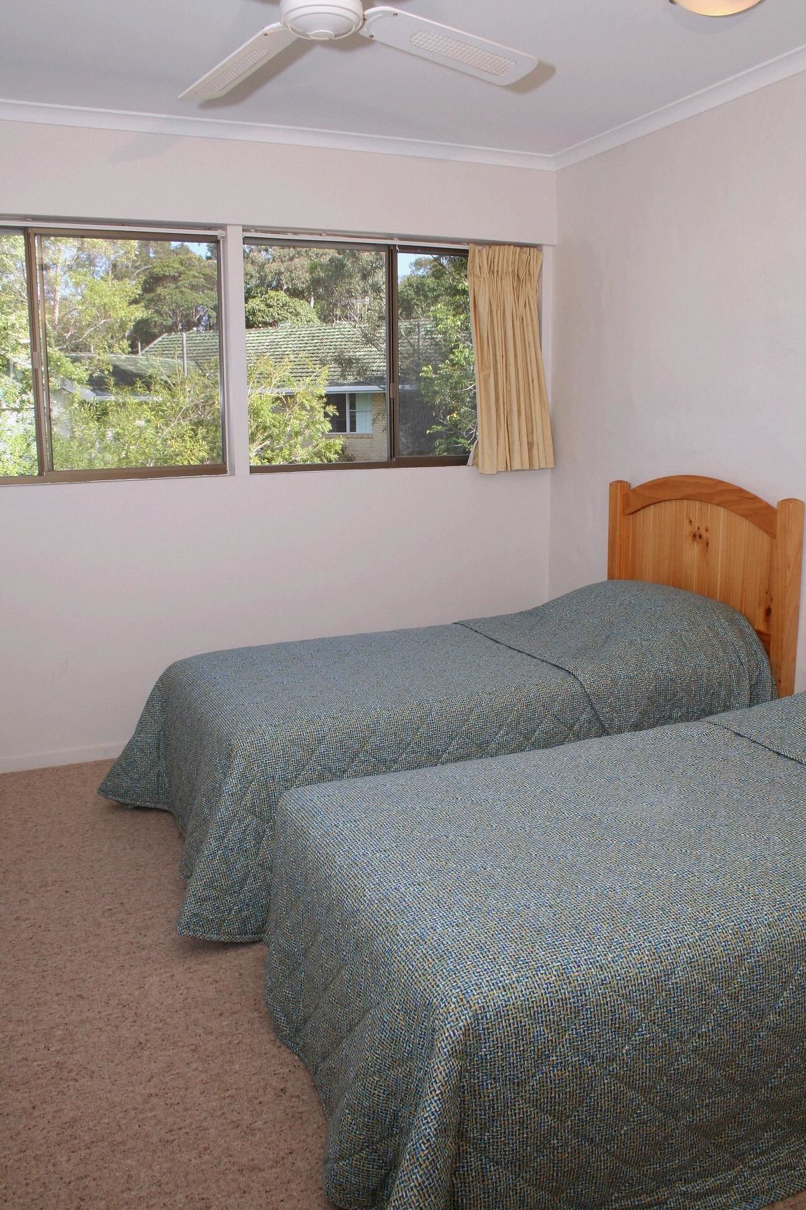 Una habitación con dos camas individuales, un ventilador de techo y una ventana con cortinas.