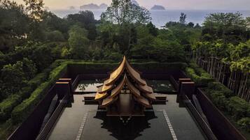 Un pavillon traditionnel dont l’image se reflète dans un bassin, entouré d’une végétation luxuriante et offrant une vue sur une étendue d’eau parsemée d’îles lointaines.