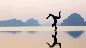 A person performing a handstand on a reflective surface with a calm body of water and distant mountains in the background.