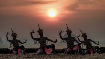 Three individuals in traditional attire seated on a flat surface with a sunset in the background.
