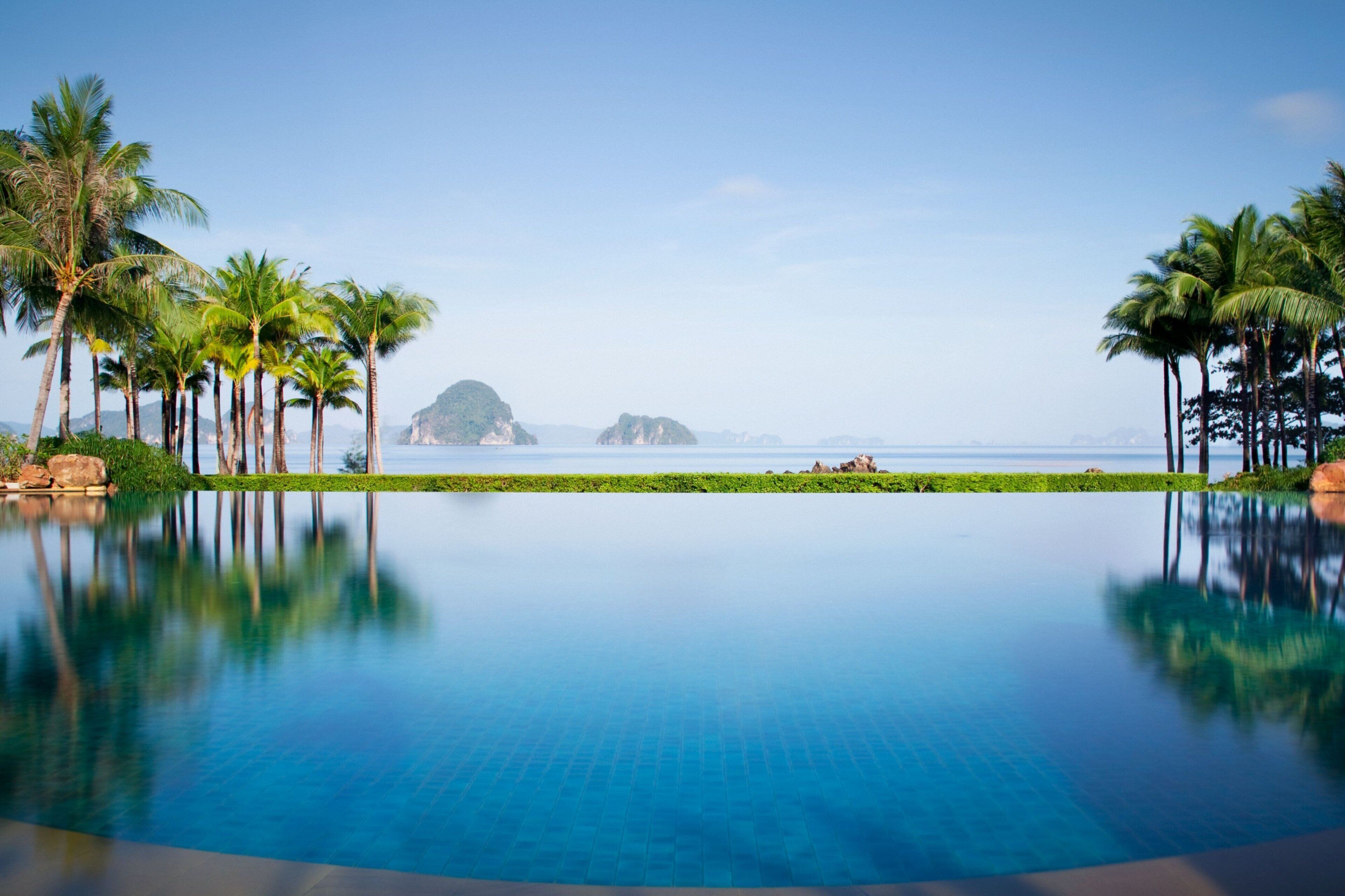 A clear blue infinity pool with a view of the ocean and palm trees.