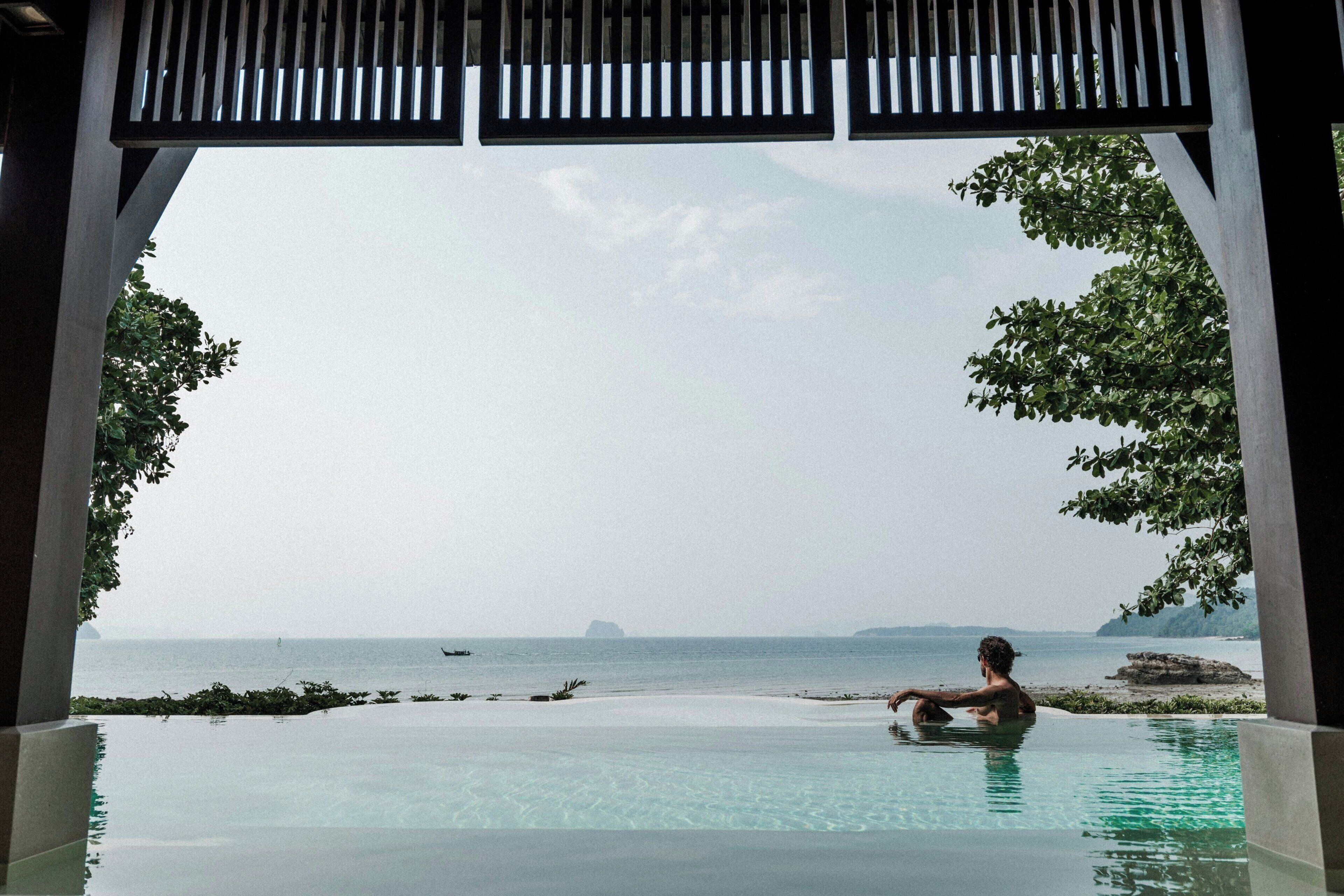 Una persona en una piscina infinita transparente con vista al mar y una isla distante.
