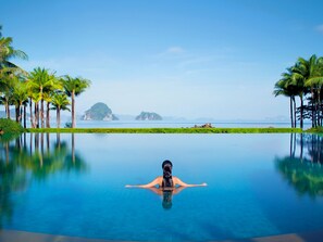 A woman relaxing in a clear infinity pool with a view of the ocean and palm trees. - Phulay Bay, a Ritz-Carlton Reserve (Krabi)
